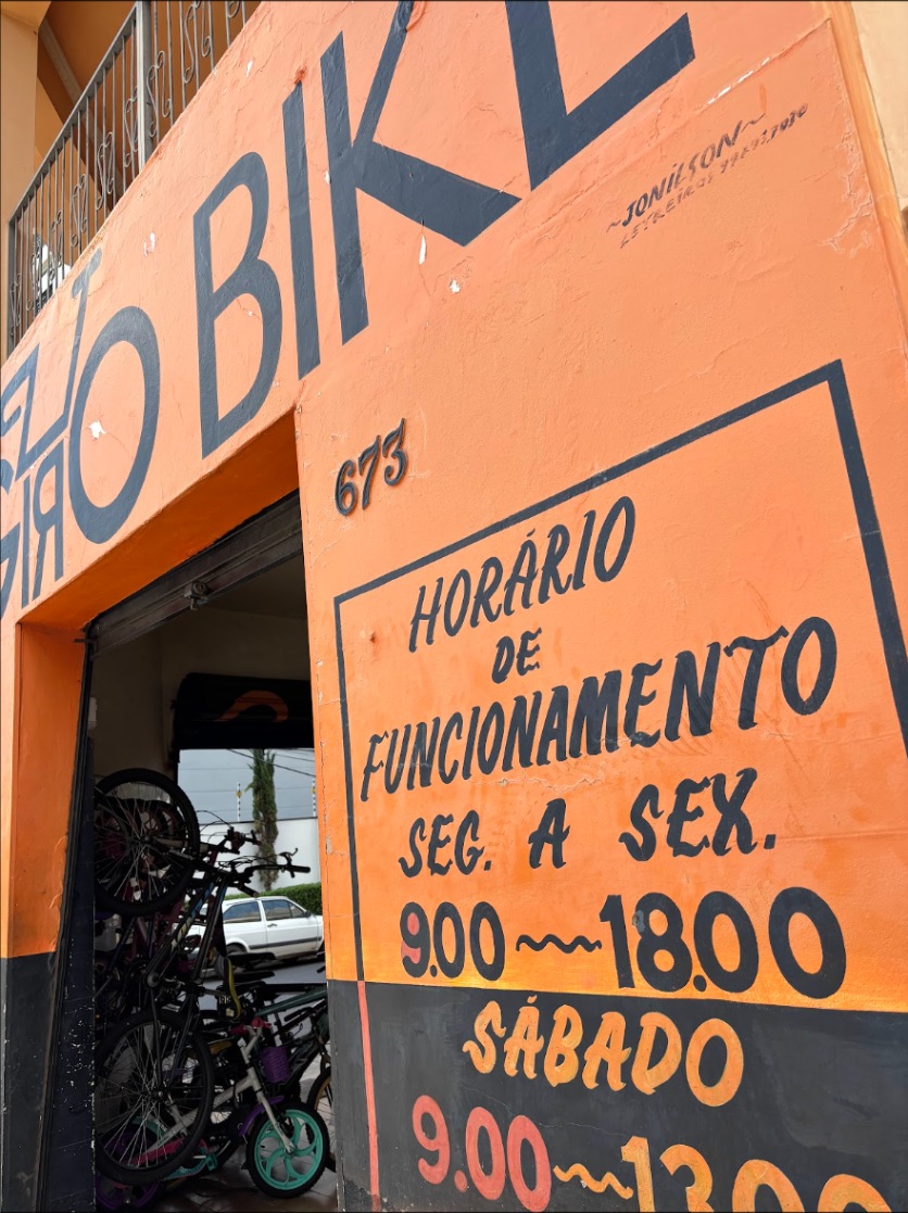 Horário de funcionamento pintado a pincel na parede laranja do endereço antigo: segunda a sexta das 9 às 18, sábado das 9 às 13